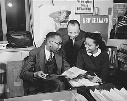 Office of War Information news bureau. Ted Poston, Negro desk editor of the Office of War Information (OWI), discusses a letter from one of the 240 Negro editors to which he sends war news from Washington, with William Clark and Harriette Easterlin, his assistants, photo by Alfred T. Palmer, 1943.